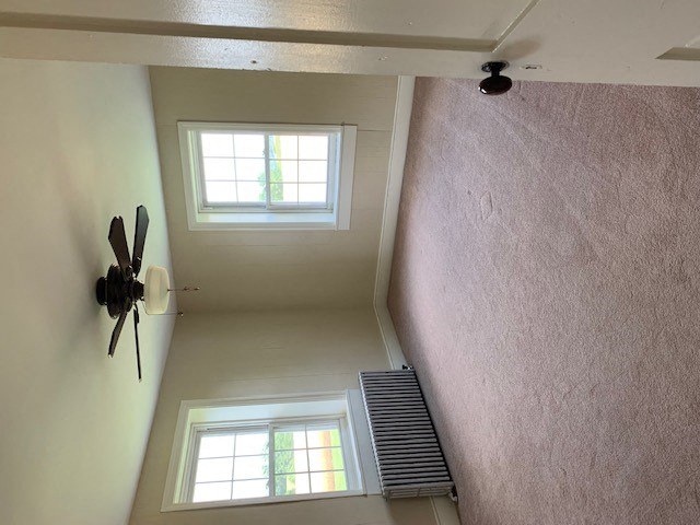 A ceiling fan is mounted on a white wall in a room with two windows.